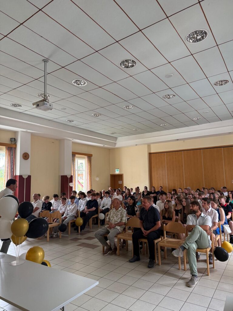 Schüler und Gäste sitzen bei einer Zeremonie in einem Saal in Österreich.